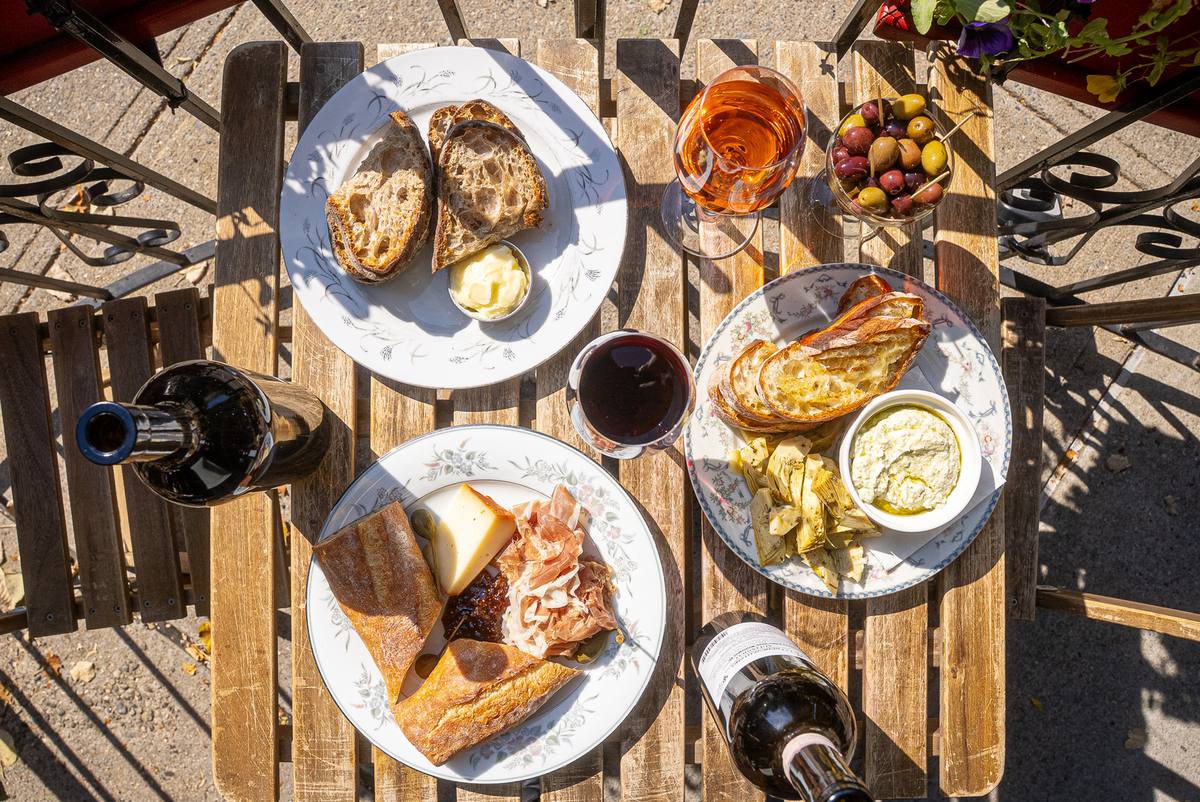 Overhead view of natural wine, bread, cheese, charcuterie and olives on an outdoor table at Pinkerton Wine Bar, Williamsburg